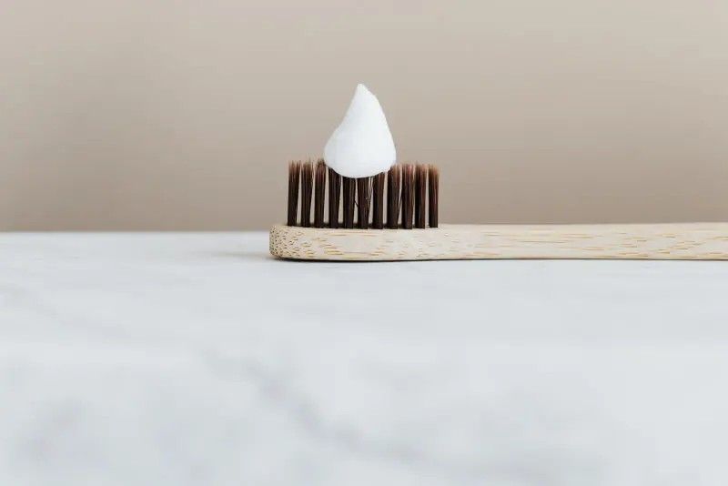 Brosse à dents en bambou portant une petite dose de dentifrice blanc, posée sur un plan en marbre clair
