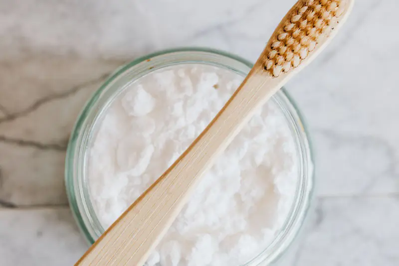 Brosse à dents en bambou posée en travers d’un bocal de poudre blanche, sur un marbre clair, comme pour un brossage maison