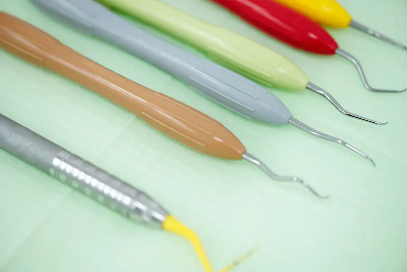 Curettes parodontales à manches colorés alignées sur un champ vert pâle, instruments du détartrage et du surfaçage
