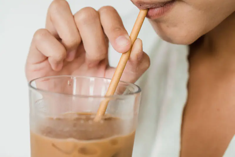 Femme buvant un café glacé à la paille, bas du visage et verre en gros plan, dans une lumière claire et douce