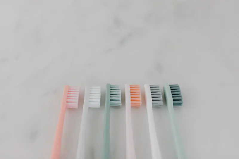 Six brosses à dents aux tons pastel, dont des verts doux, alignées côte à côte sur un plan de marbre clair