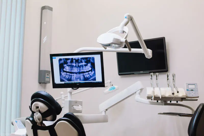 Radiographie panoramique affichée sur l’écran d’une salle de soins dentaires claire, à côté du scialytique et du fauteuil