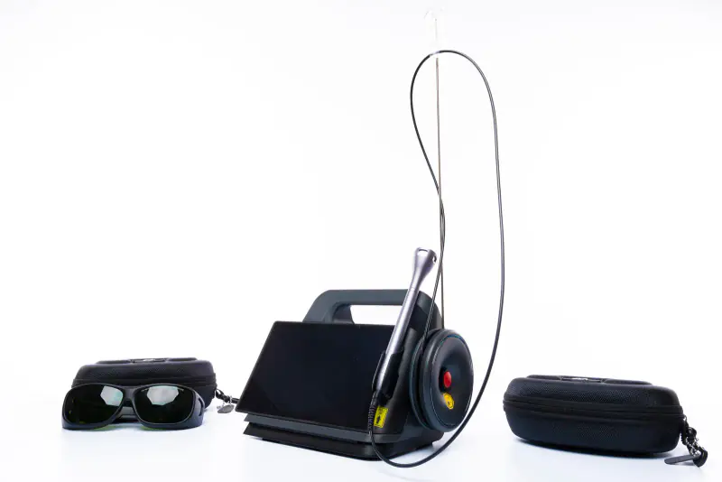 Laser dentaire portable avec sa pièce à main, ses lunettes de protection et ses étuis de rangement, sur un fond blanc