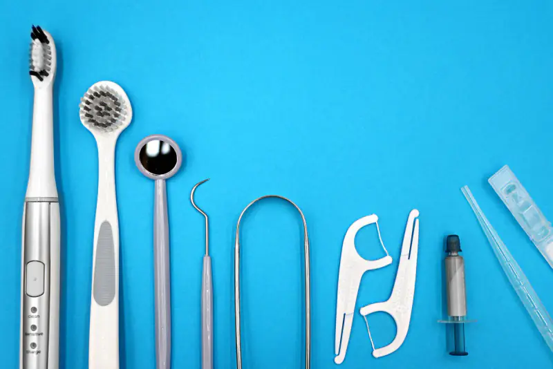 Brosse à dents électrique, brosse et gratte-langue, miroir, sonde et porte-fils dentaires alignés sur un fond bleu