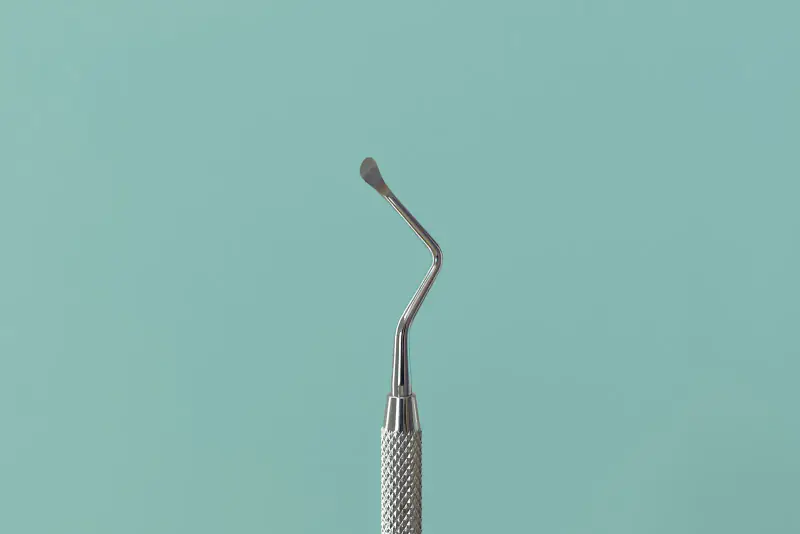 Instrument dentaire en acier à petite spatule recourbée, du type utilisé pour mettre en place une obturation, sur un fond vert d'eau