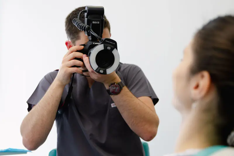 Praticien tenant un appareil reflex équipé d’un flash annulaire macro, prêt à photographier une patiente vue de dos