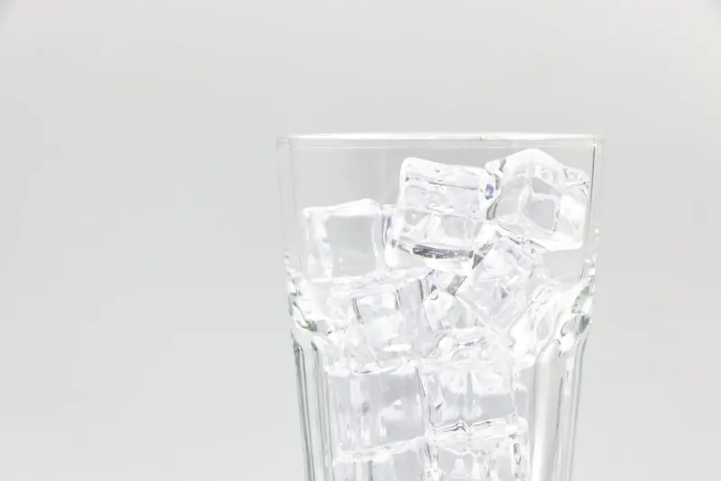 Verre rempli de glaçons sur fond gris très clair, évoquant le froid qui déclenche la sensibilité dentaire