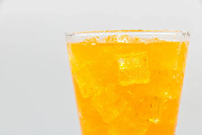 Verre d’une boisson orange pétillante avec des glaçons et de fines bulles, photographié en gros plan sur un fond clair
