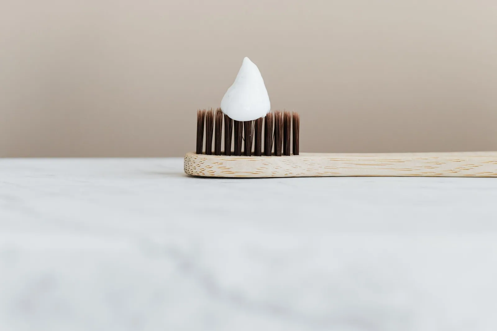 Brosse à dents en bambou portant une petite dose de dentifrice blanc, posée sur un plan en marbre clair