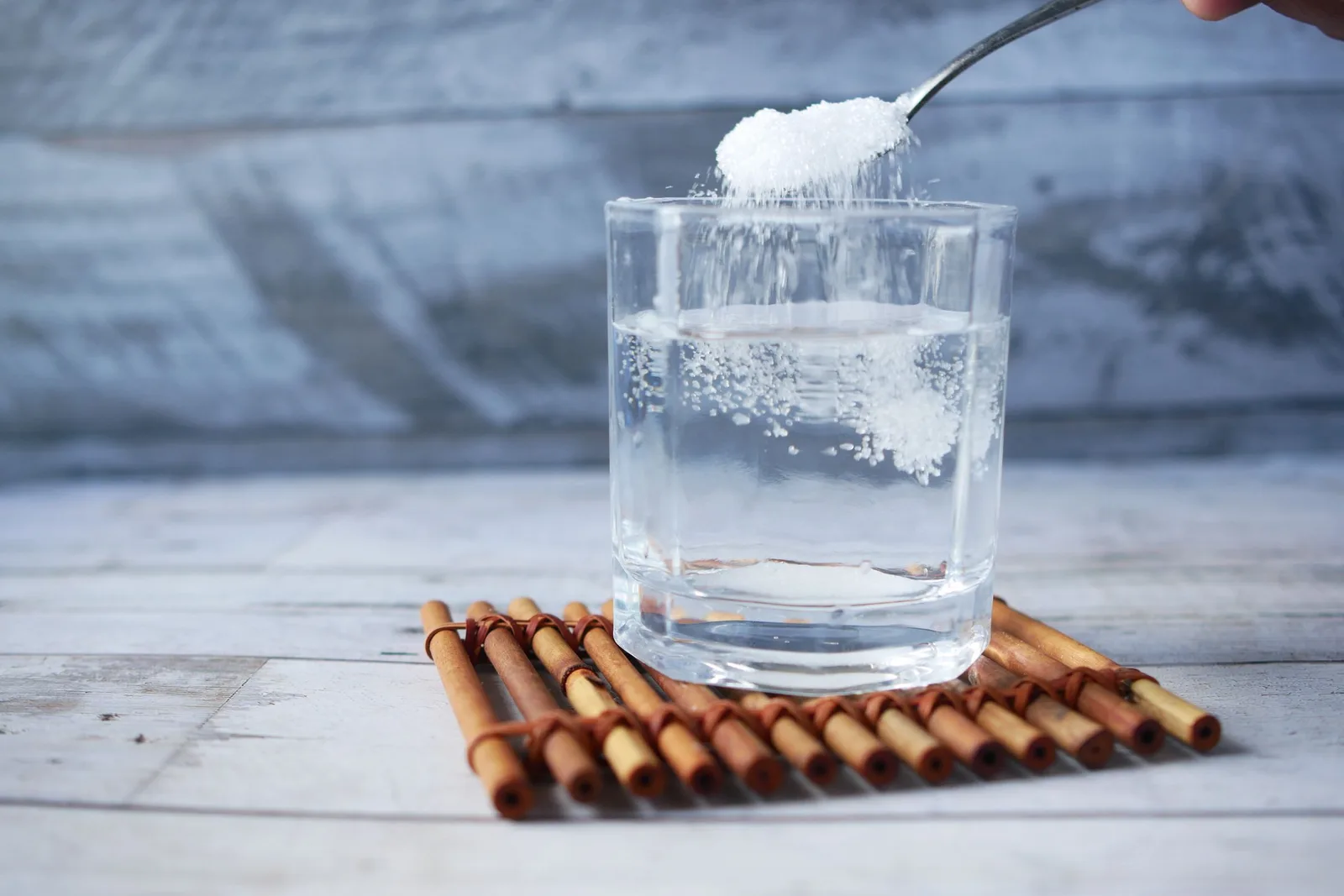 Cuillère versant une poudre blanche dans un verre d'eau posé sur un dessous-de-verre en bambou