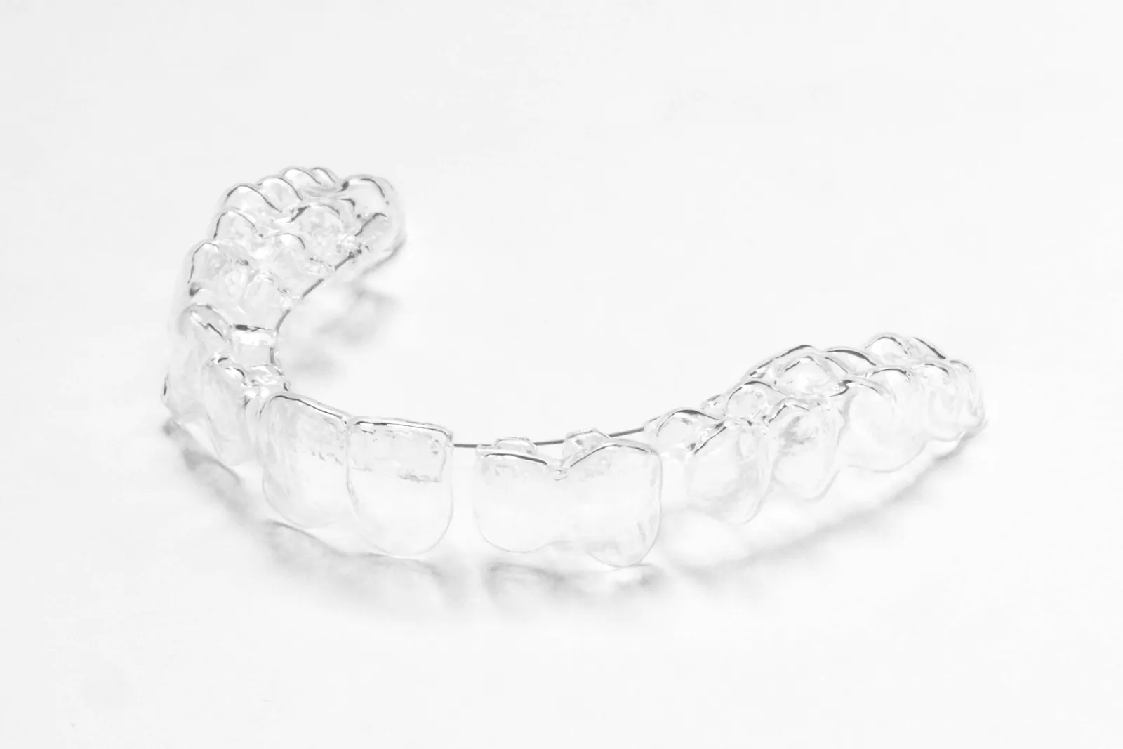 Transparenter kieferorthopädischer Aligner allein auf einer weißen Fläche, in weichem Licht fotografiert