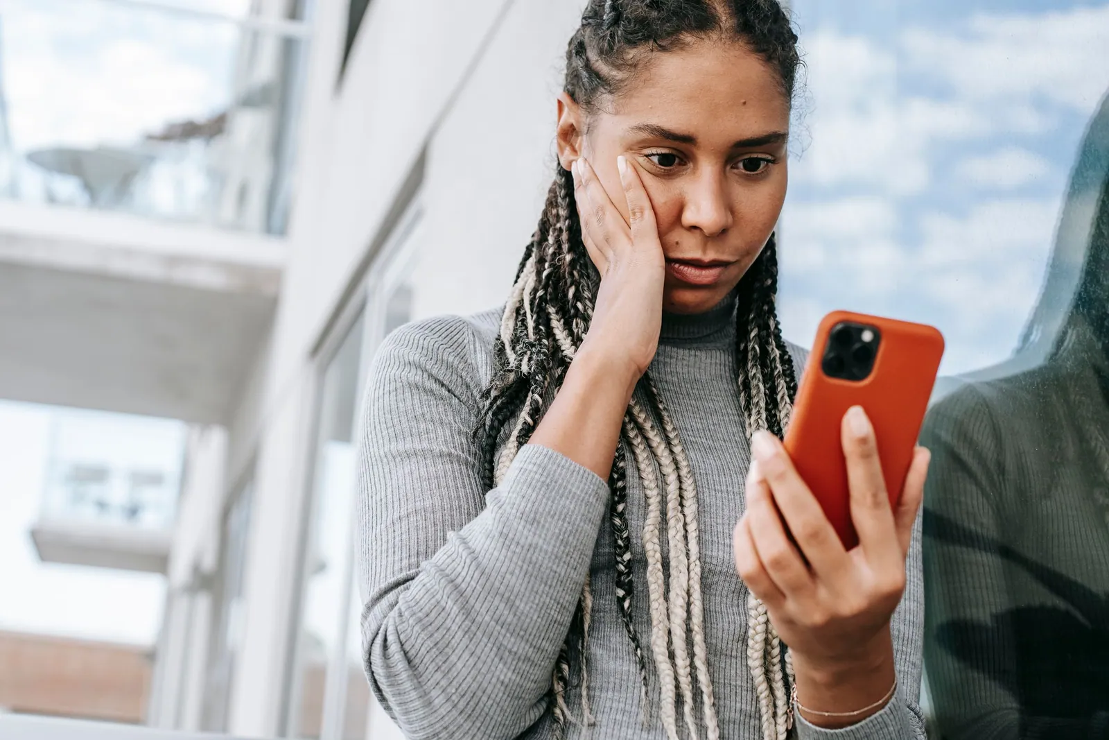 Femme inquiète, la main posée sur la joue, qui regarde son smartphone, comme au moment de chercher qui appeler