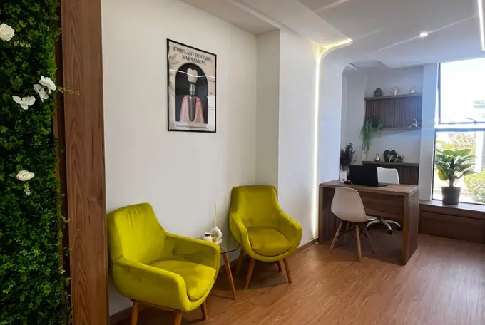 Coin d'attente du cabinet devant un mur végétal, fauteuil vert anis et fenêtre lumineuse