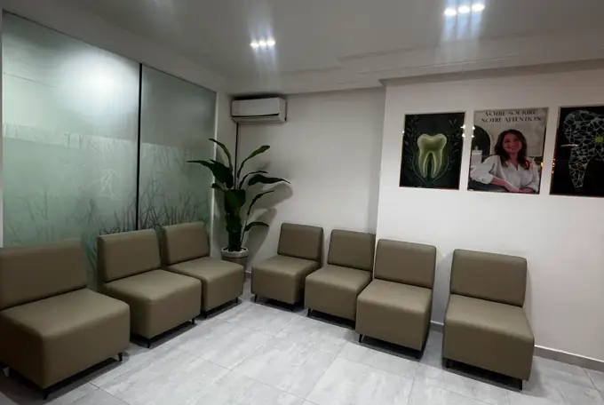 Salle d'attente du cabinet dentaire : rangée de fauteuils beiges, plante verte et affiches encadrées