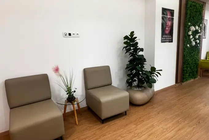 Espace d'attente du cabinet dentaire avec deux fauteuils beiges et plantes d'intérieur à Kénitra